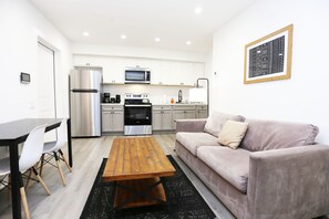A modern kitchen with white cabinets, stainless steel appliances, and a wooden dining table with chairs. - Petworth Luxury Unit with Modern Comforts (Washington)