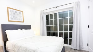 A bedroom with a large bed, a headboard, a nightstand, a window with curtains, and a framed picture on the wall. - Petworth Luxury Unit with Modern Comforts (Washington)