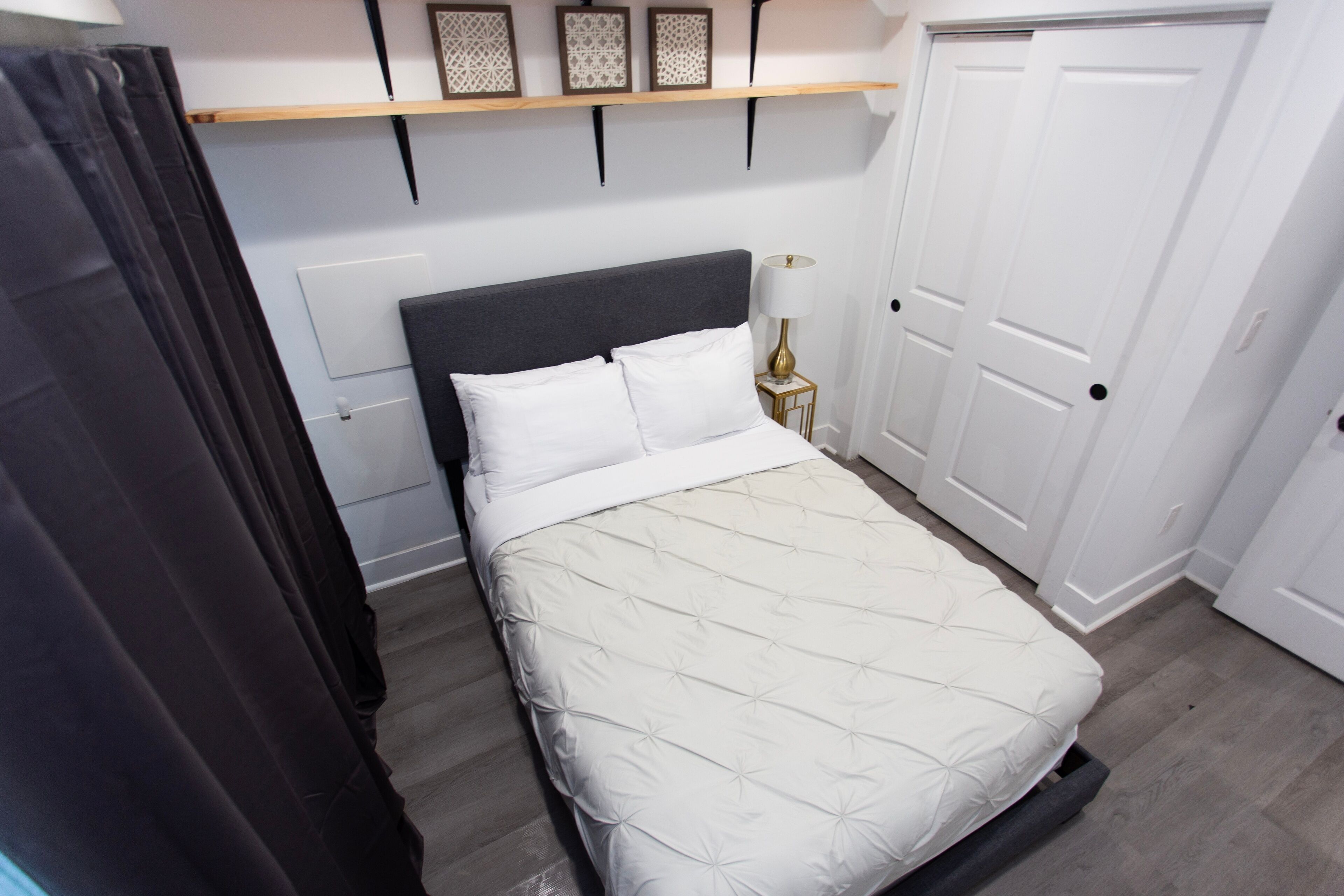 Una cama bien tendida con un edredón blanco, una lámpara de noche y un estante de madera encima.