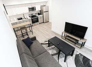 Un appartement moderne comprenant une cuisine, un espace de vie avec un canapé et un téléviseur, ainsi qu’une table à manger.