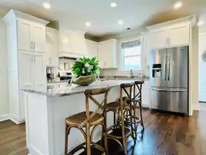 A modern kitchen with white cabinets, a stainless steel refrigerator, and a central island with bar stools. - The Hughes, 3BR Timeless Stay by VelvetDitchVillas (Oxford)
