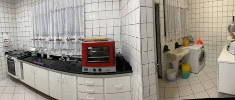 A kitchen with white cabinets, a red oven, a sink, and a window with lace curtains.
