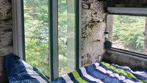 Habitació rústica amb un llit, una finestra i vistes als arbres.
