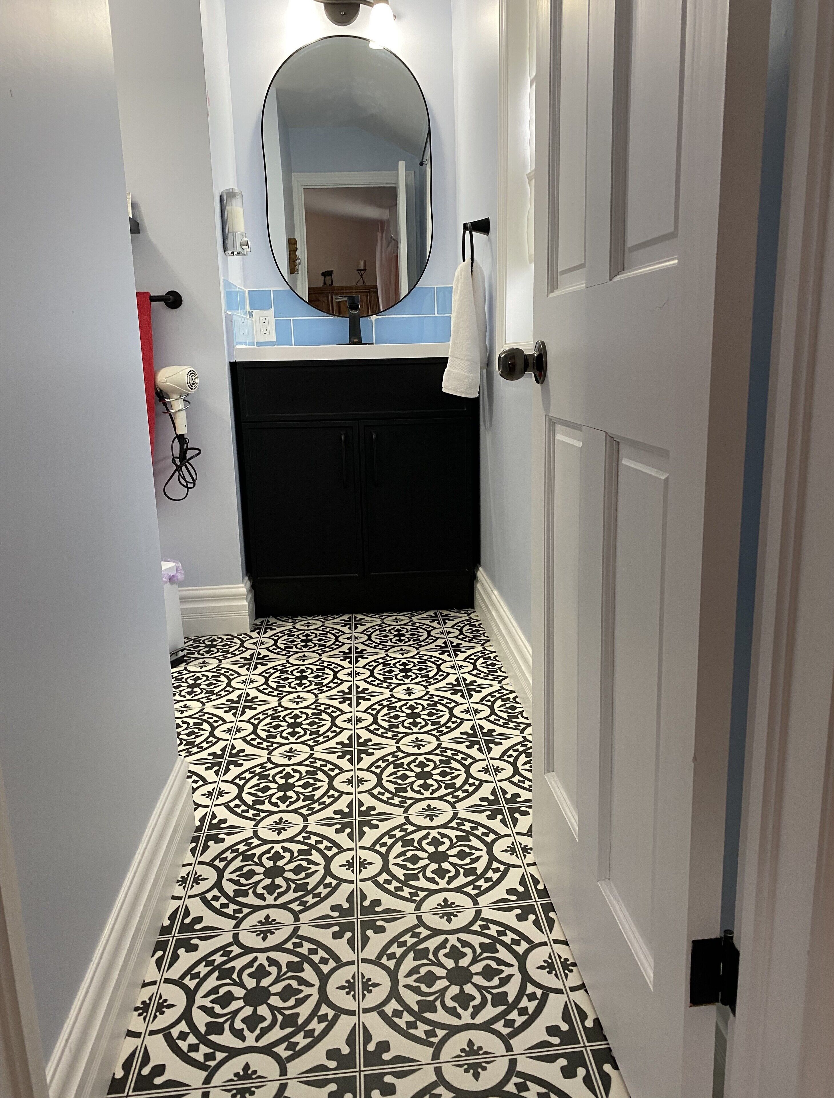 Une salle de bain avec un carrelage noir et blanc, une porte blanche et un miroir au-dessus du lavabo.