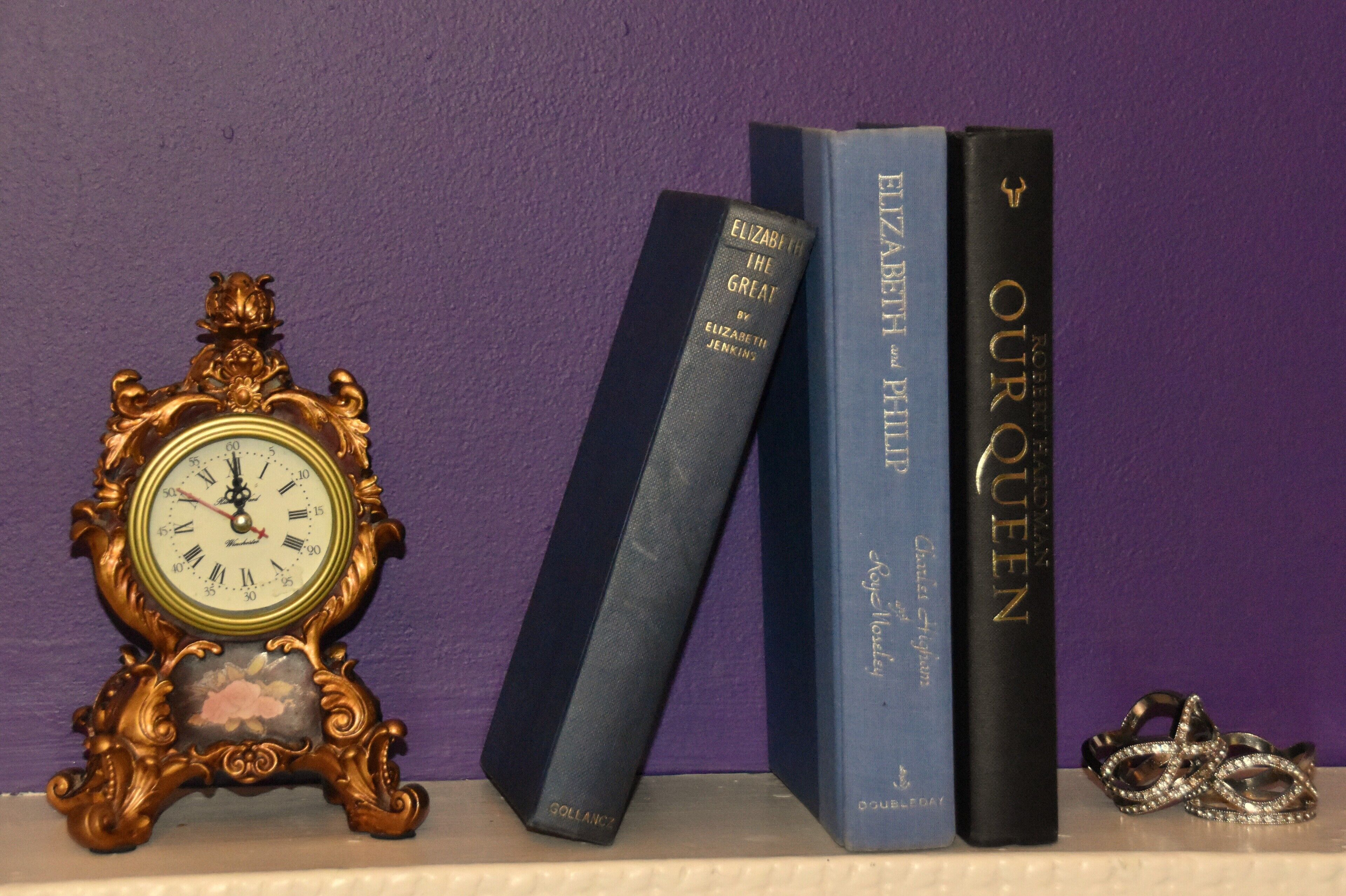 A clock, three books, and a pair of rings on a shelf.