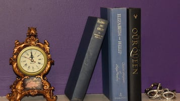 A clock, three books, and a pair of rings on a shelf.