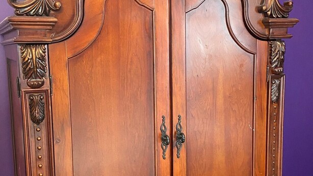 A wooden wardrobe with two doors and a lower cabinet, featuring ornate carvings and brass handles. - Seabank House Bed and Breakfast (Pictou)