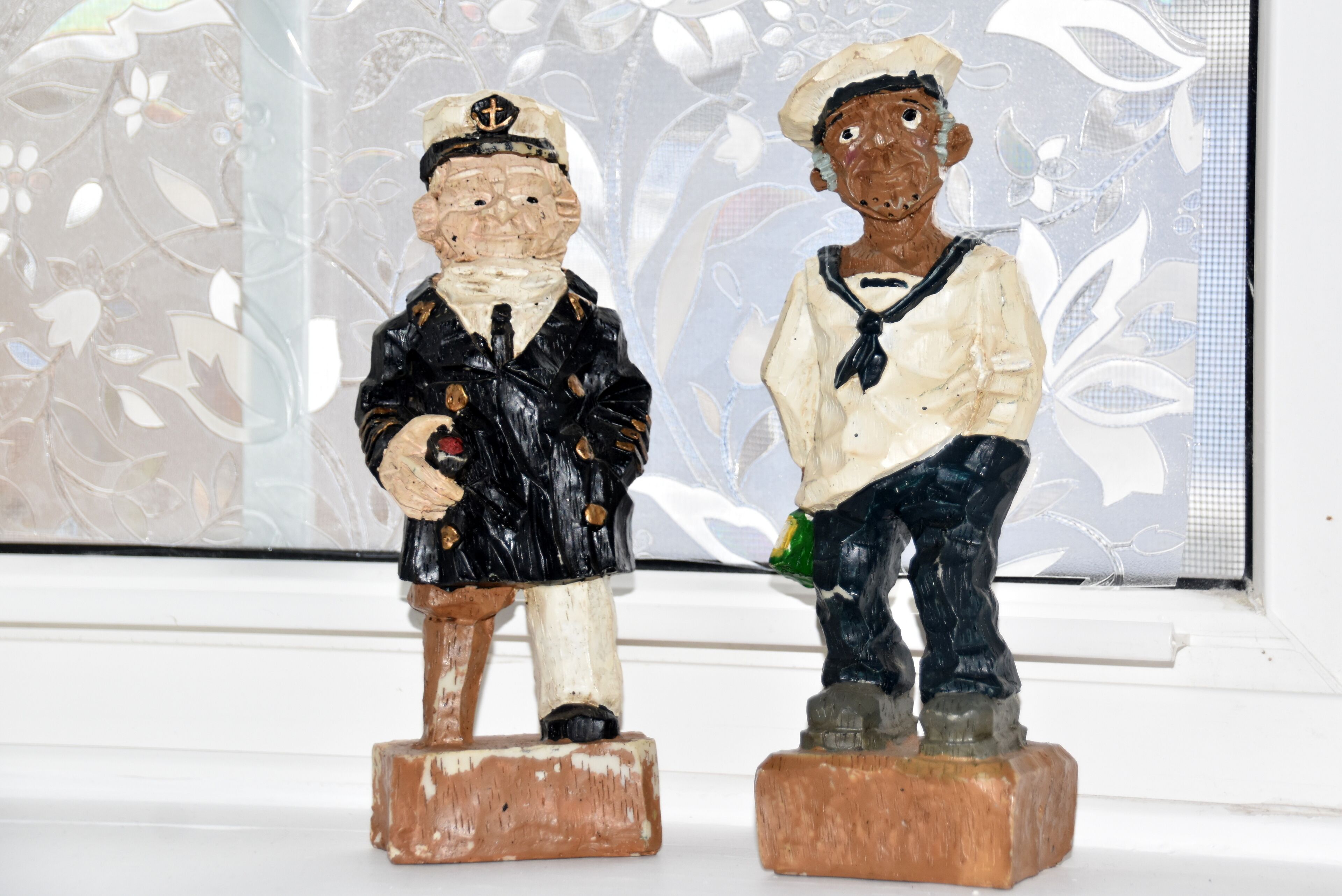 Dos figuras de madera de marineros sobre una superficie blanca.