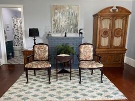 Una sala de estar con dos sillones estampados con flores, una mesita, una chimenea y un aparador de madera.