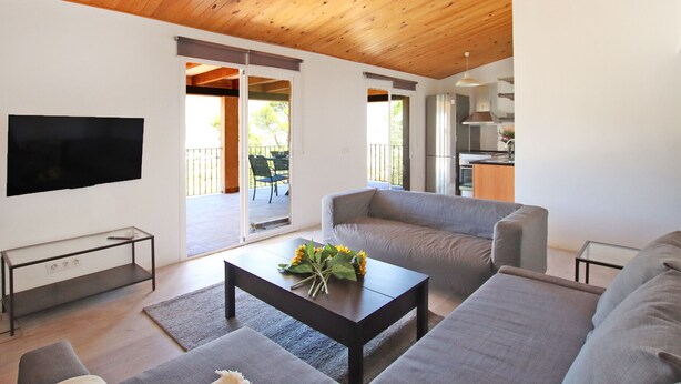 A modern living room with a wooden ceiling, a flat-screen TV, a grey sofa, and a coffee table with a flower arrangement. - Villa Ses Costes with private pool, garden and panoramic views of the mountains in Alaró  (Alaro)