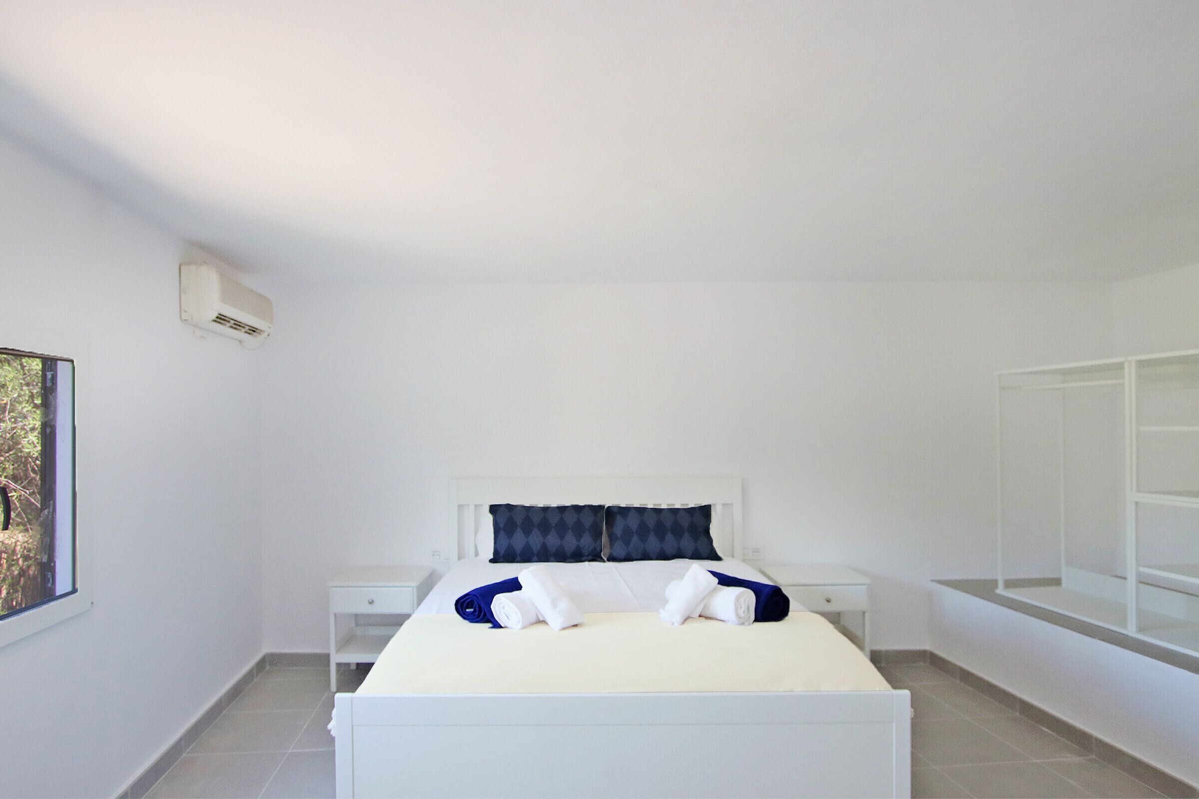 A clean, modern hotel room with a bed, two nightstands, a window, and a built-in wardrobe.