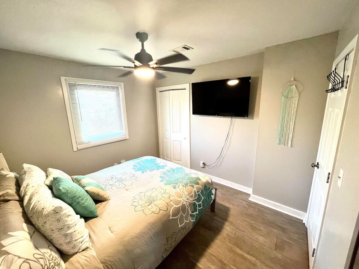 A bedroom with a bed, ceiling fan, TV, and a door with a coat rack.