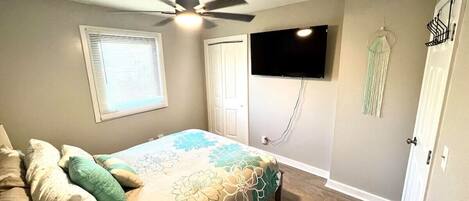 A bedroom with a bed, ceiling fan, TV, and a door with a coat rack.