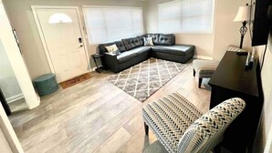 A living room with a sectional sofa, a patterned rug, a ceiling fan, and a small table with a lamp.