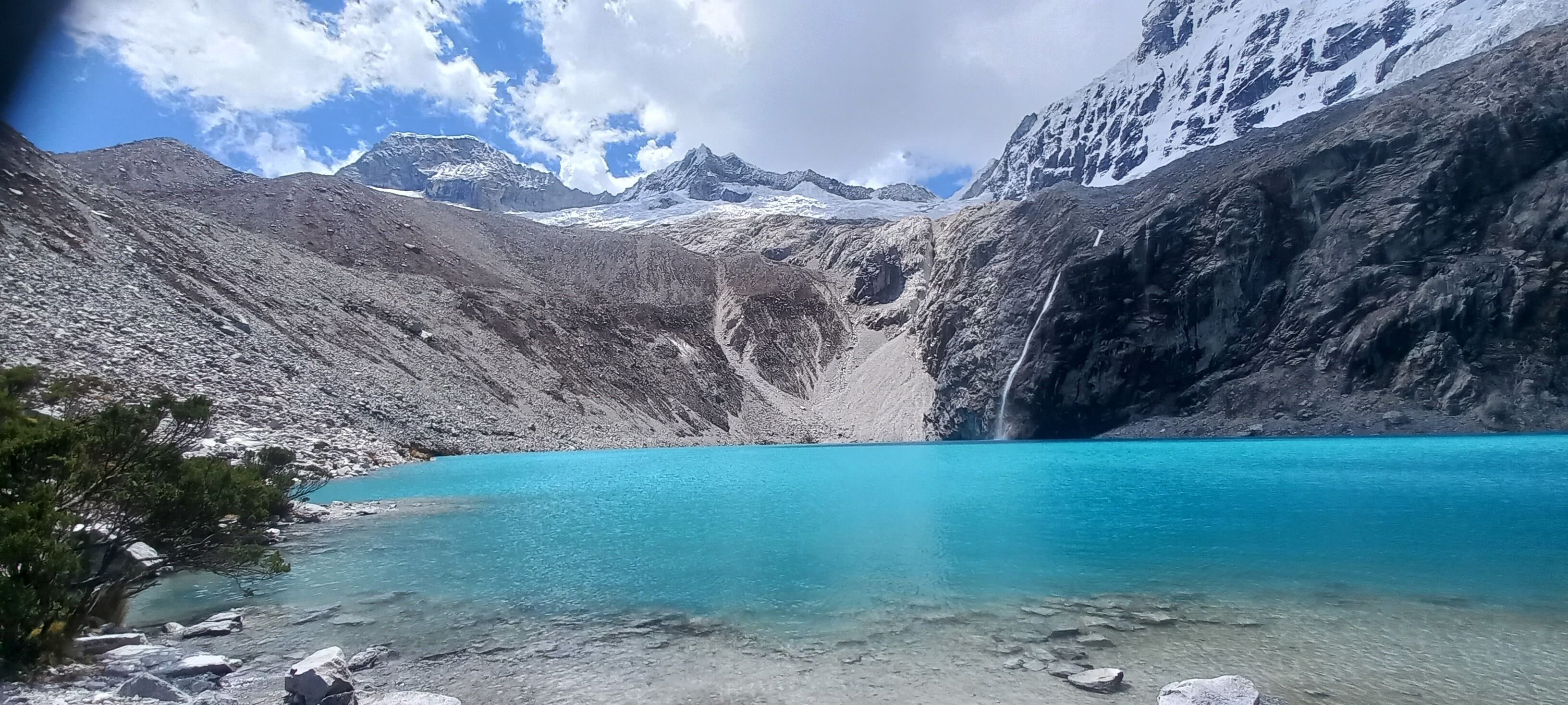 A mountainous landscape with a clear turquoise lake, rocky terrain, and snow-capped peaks in the background.