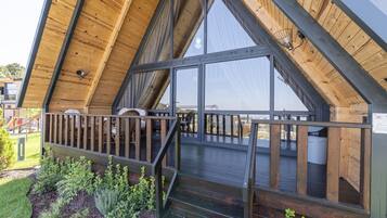 A wooden deck with a railing, a staircase, and a view of the interior through large windows.