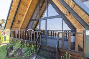Una terraza de madera con barandilla, una escalera y vistas al interior a través de amplios ventanales.