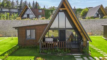 A modern A-frame house with a balcony, surrounded by a well-maintained lawn and a stone wall.