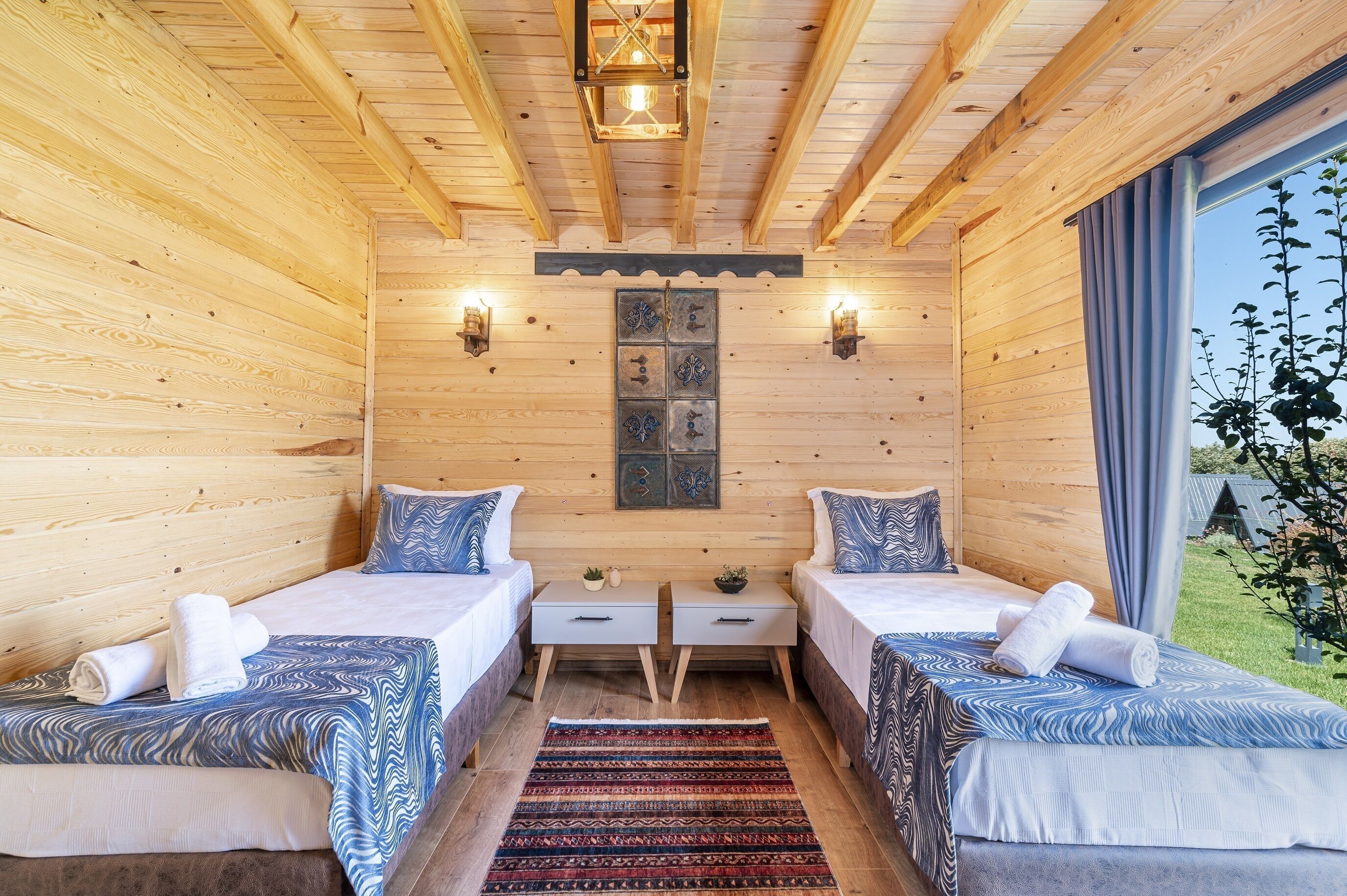 Una habitación tipo cabaña de madera con dos camas, una mesita pequeña y dos luces fijadas a la pared.