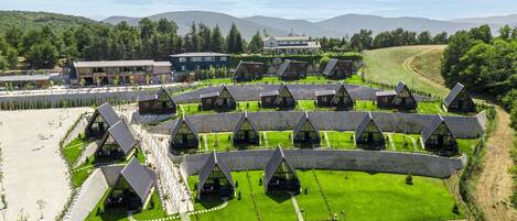 A modern resort with multiple triangular-roofed cabins arranged in rows, surrounded by well-maintained lawns and pathways.