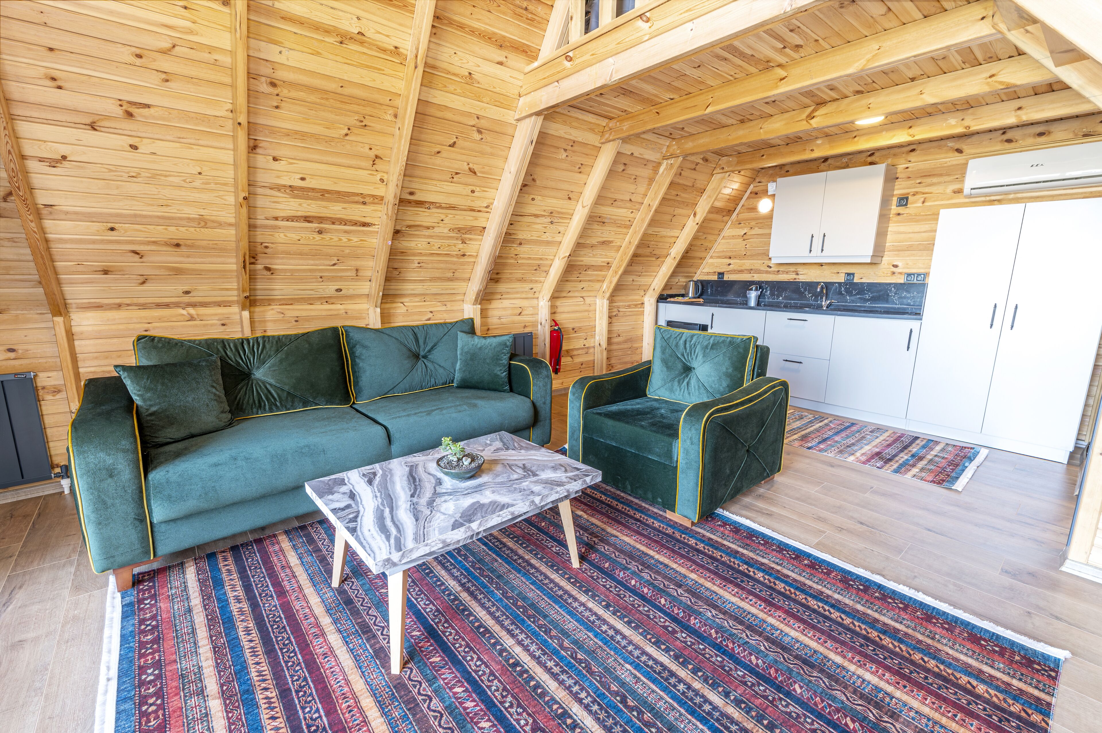 A cozy loft-style room with a wooden ceiling, a green sofa, a matching armchair, and a marble coffee table.