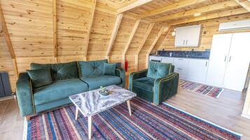 A cozy loft-style room with a wooden ceiling, a green sofa, a matching armchair, and a marble coffee table.