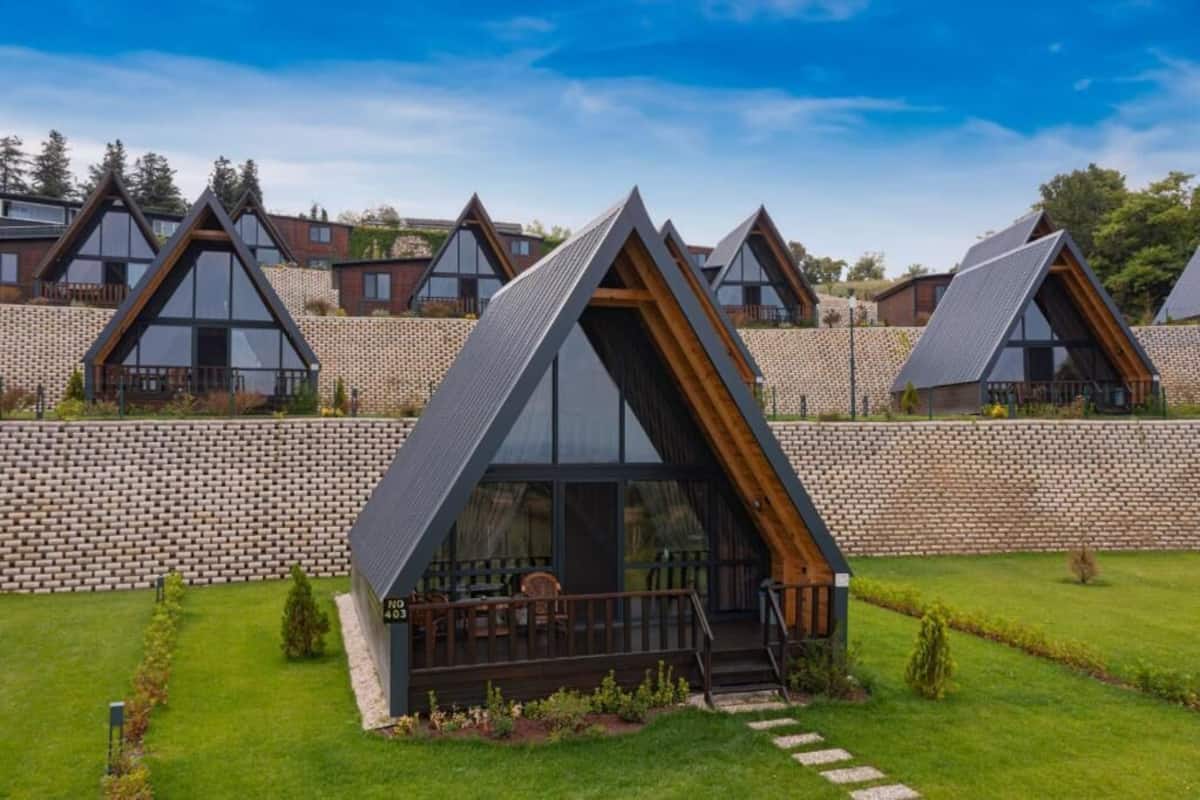 Una hilera de cabañas modernas con techos triangulares, ventanas grandes, un muro de ladrillo y un césped.