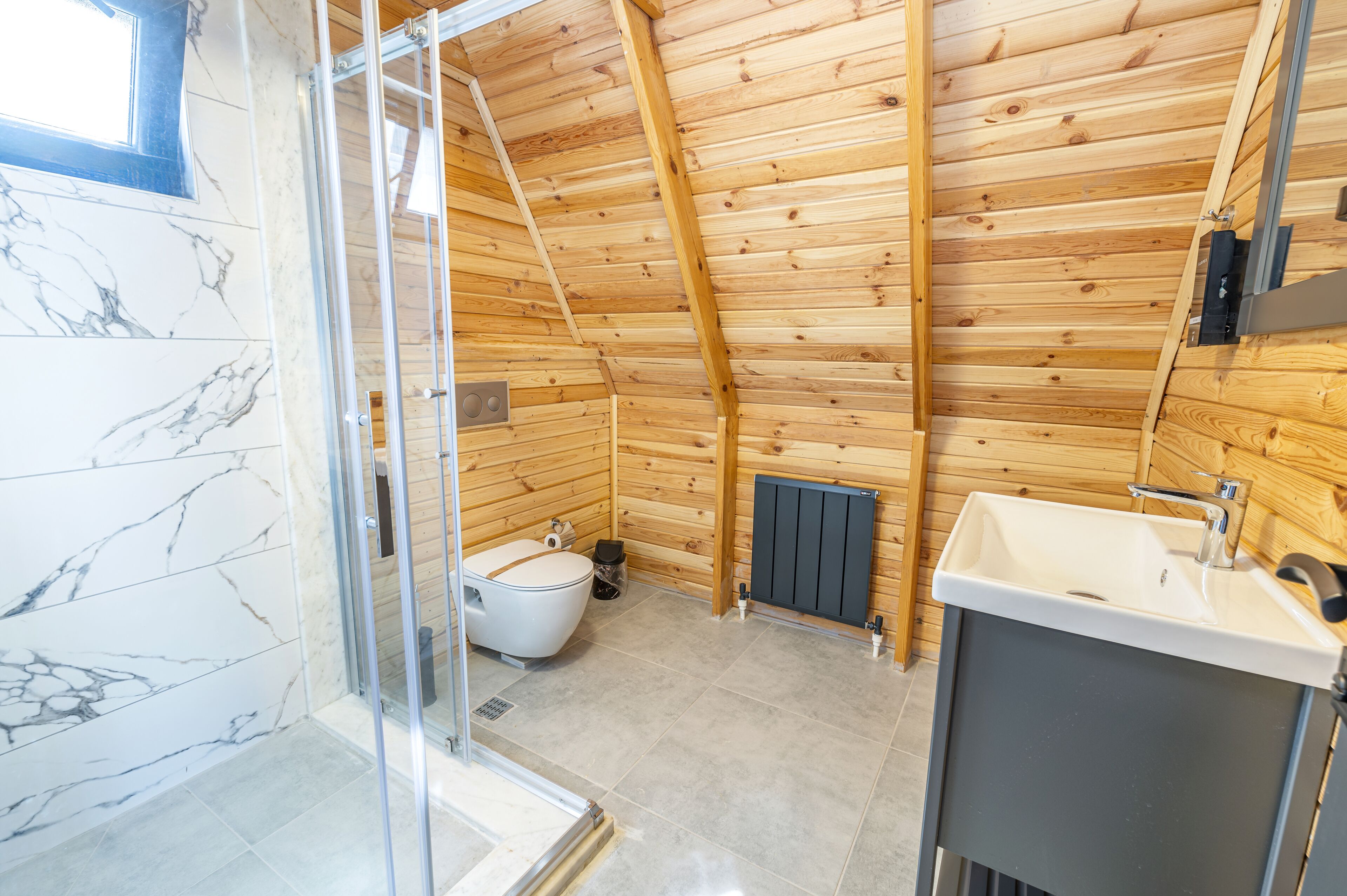 Puupaneloitu kylpyhuone, jossa on wc, pesuallas ja suihkutila.