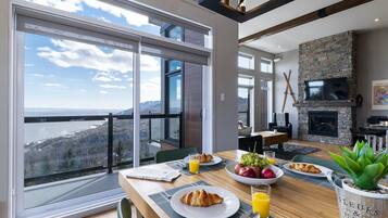 A dining area with a table set for breakfast, a fireplace, and a scenic view through large windows.