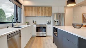A modern kitchen with a dishwasher, oven, and refrigerator, wooden cabinets, and a large window.