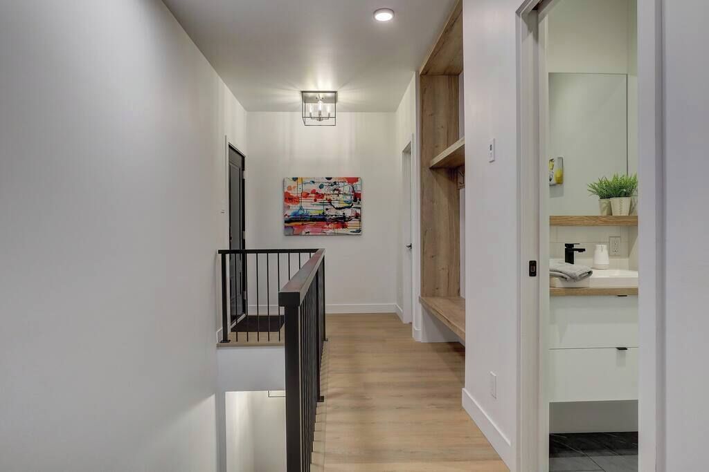 A modern hallway with a wooden floor, a black railing, and a painting on the wall.