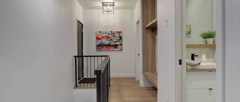 A modern hallway with a wooden floor, a black railing, and a painting on the wall.