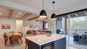 A modern kitchen with a central island, pendant lighting, and a dining area with a wooden table and chairs.