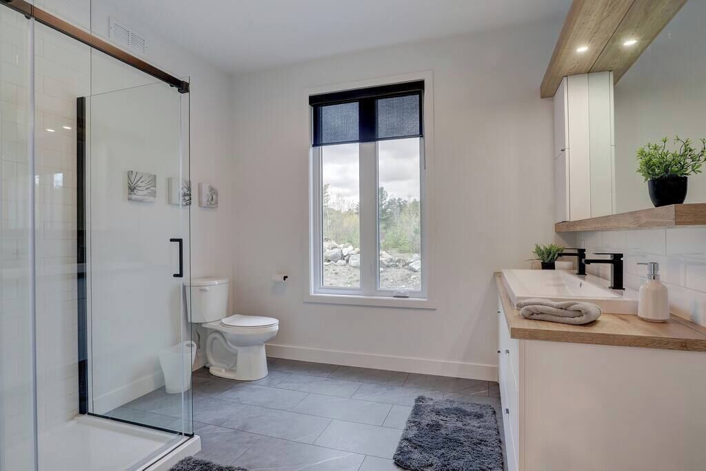 Un bagno moderno con box doccia in vetro, un water, un lavabo con piano in legno e una finestra che offre luce naturale.