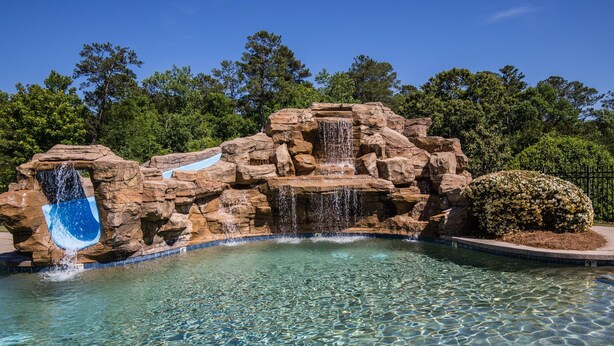 Una piscina trasparente con una cascata rocciosa e uno scivolo blu.