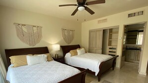 Una camera d'albergo con due letti, una ventola a soffitto, un comodino con una lampada e vista sulla cucina.