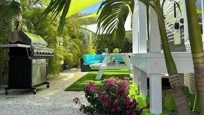 A patio area with a grill, outdoor furniture, and a small garden with pink flowers. - The Lazy Turtle Inn + Beach & Pool (Key Largo)