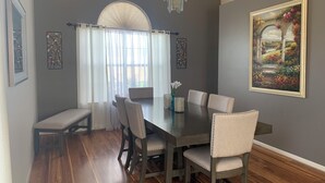 A dining room with a dark wooden table, six chairs, a bench, a chandelier, and a painting on the wall. - 3 Bed Desert Beach House with a Mountain View - Private Pool and Hot Tub! (Rio Rancho)