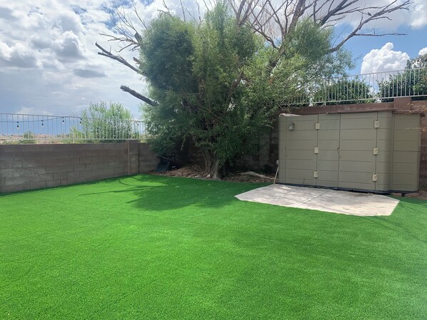 A backyard with artificial green turf, a metal gate, and a tree.