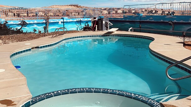 A swimming pool with a tiled edge, a hot tub, and a view of a desert landscape with buildings in the background. - 3 Bed Desert Beach House with a Mountain View - Private Pool and Hot Tub! (Rio Rancho)