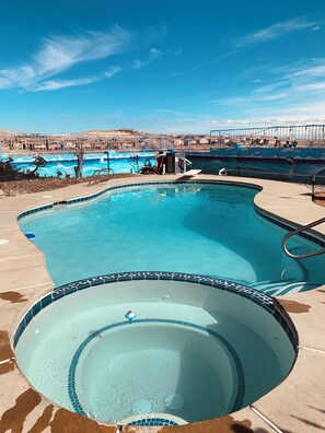 A swimming pool with a tiled edge, a hot tub, and a view of a desert landscape with buildings in the background.
