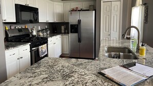 A kitchen with white cabinets, a stainless steel refrigerator, a black stove, and a granite countertop. - 3 Bed Desert Beach House with a Mountain View - Private Pool and Hot Tub! (Rio Rancho)