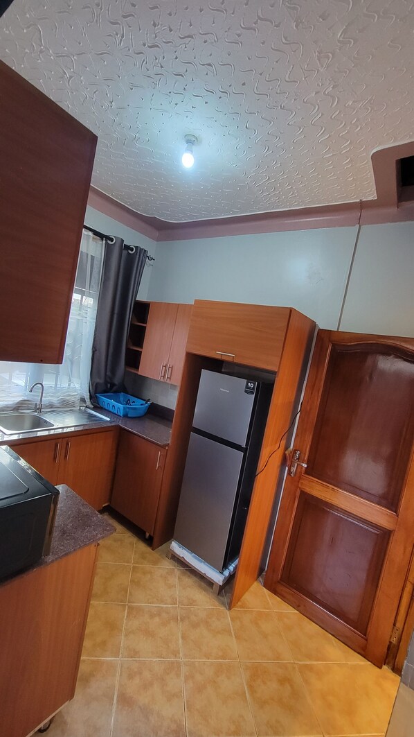 A compact kitchen with wooden cabinets, a built-in refrigerator, a sink, and a window with curtains.
