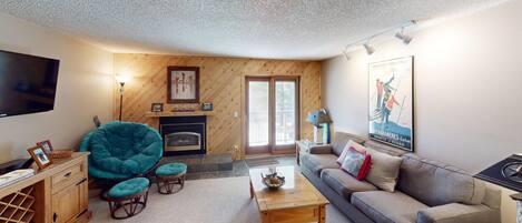 A cozy living room with a fireplace, a teal chair, a sofa, and a flat-screen TV.