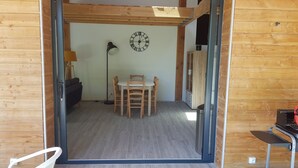 A wooden interior with a dining area, a clock on the wall, and a sliding door leading to another room. - Cevennes Nature Entourée de Végétation, à 3mn de la Rivière, à 1mn de la Piscine (Chambon)