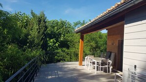 A patio with a table and chairs, surrounded by greenery and a wooden building. - Cevennes Nature Entourée de Végétation, à 3mn de la Rivière, à 1mn de la Piscine (Chambon)