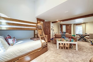 Ein Zimmer mit einem Etagenbett, einer Holzleiter, einem Sofa, einem kleinen Tisch und einem Fenster mit Vorhängen.