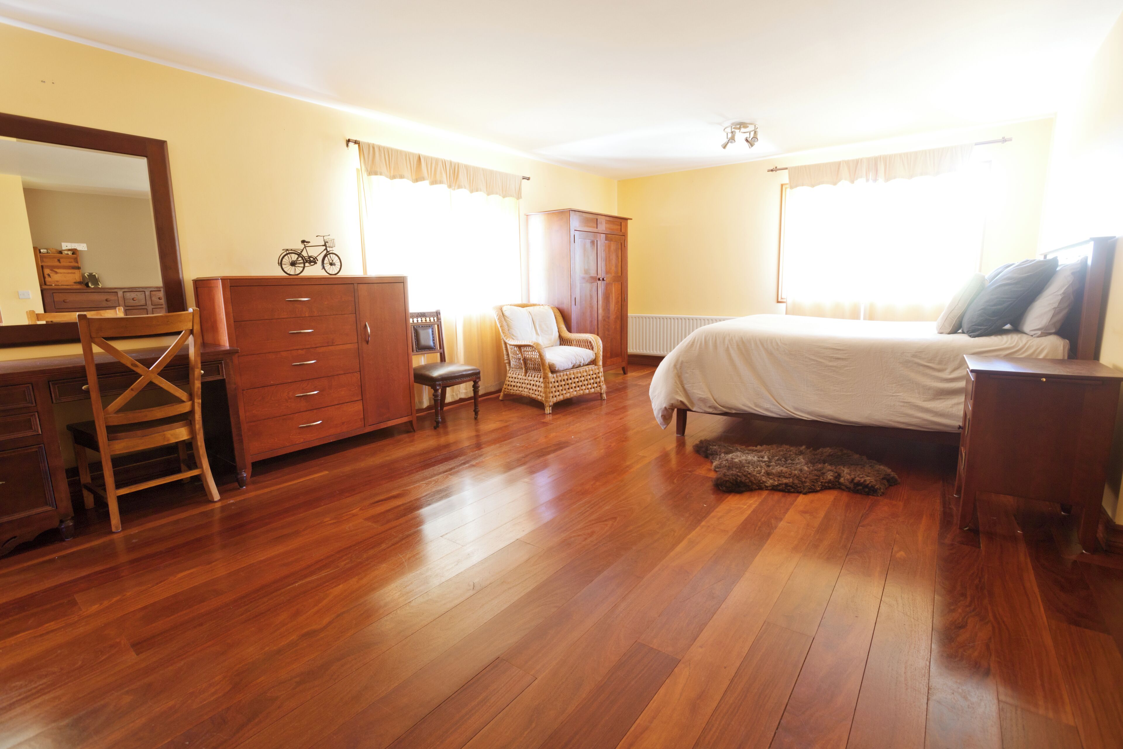 A bedroom with wooden flooring, a bed, a dresser, a chair, a wardrobe, and a mirror.