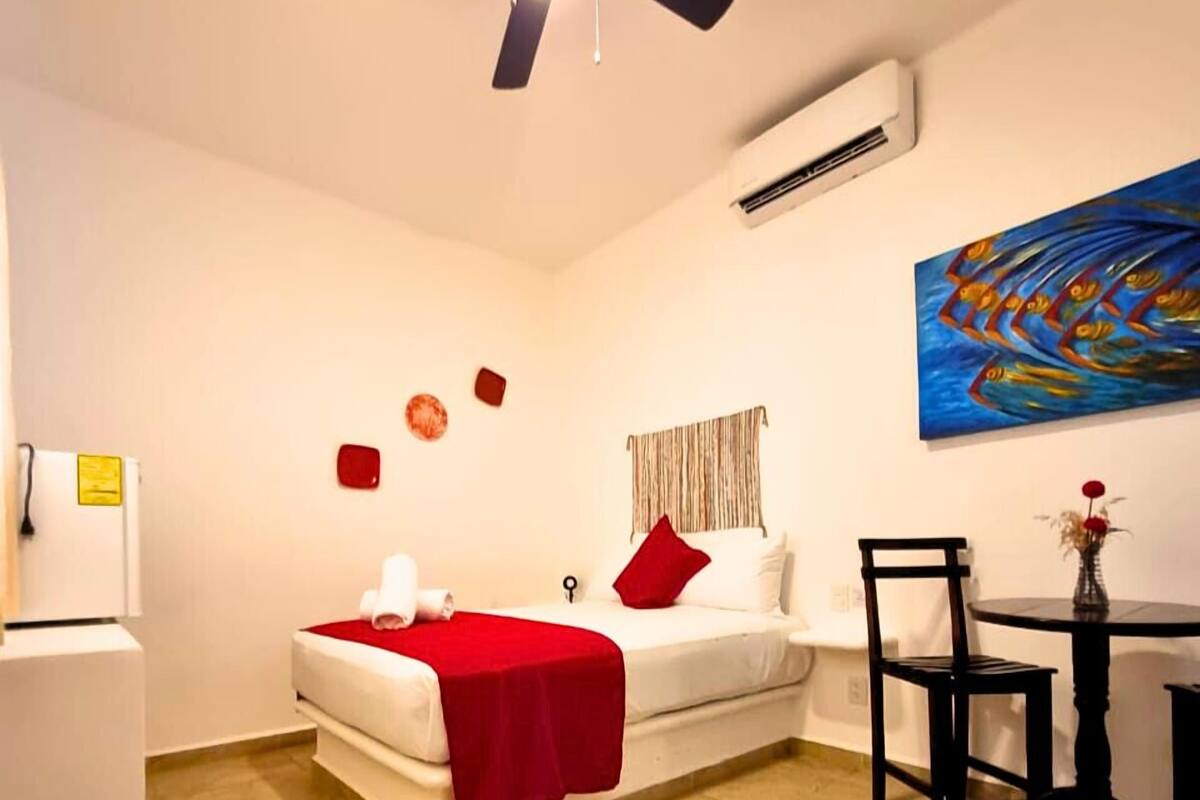 Ein Hotelzimmer mit Bett, Schreibtisch, Stuhl, Deckenventilator, Klimaanlage und einem Bild an der Wand.