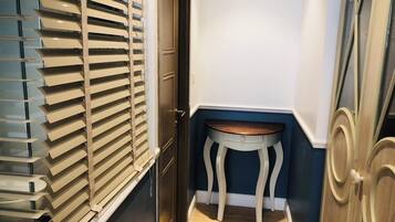 A narrow hallway with a door, a small table, and a window with blinds.